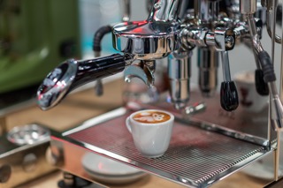 A cup of coffee with latte art beneath a Bezzera espresso machine