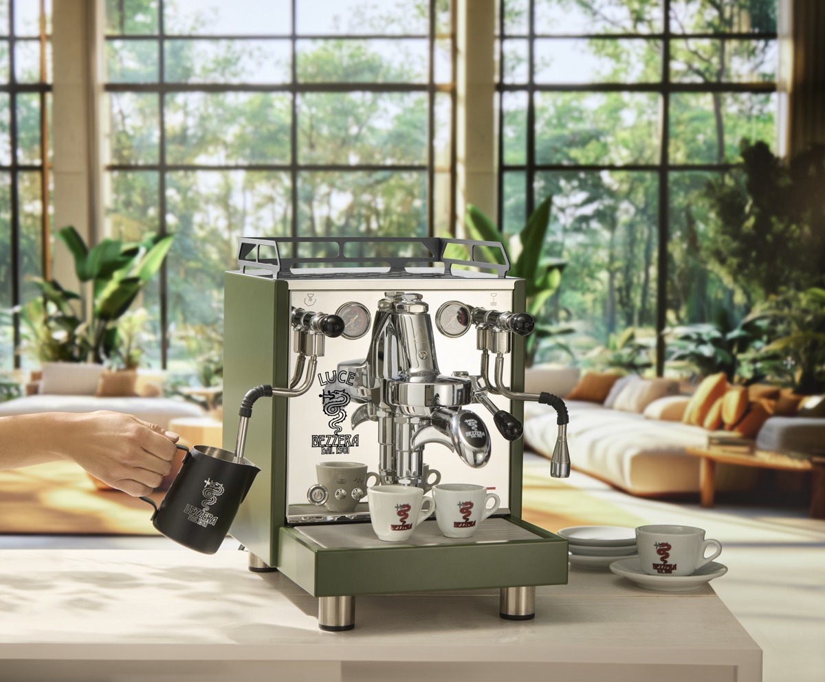 A hand holding a milk jug beneath the steam wand of a green Bezzera Luce