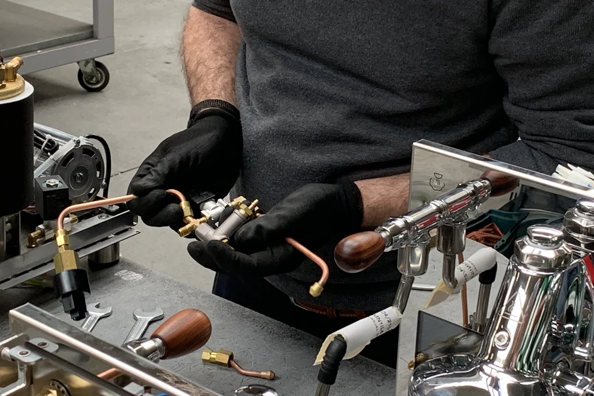 A craftsperson assembles copper and brass components inside a Bezzera espresso machine at the factory.